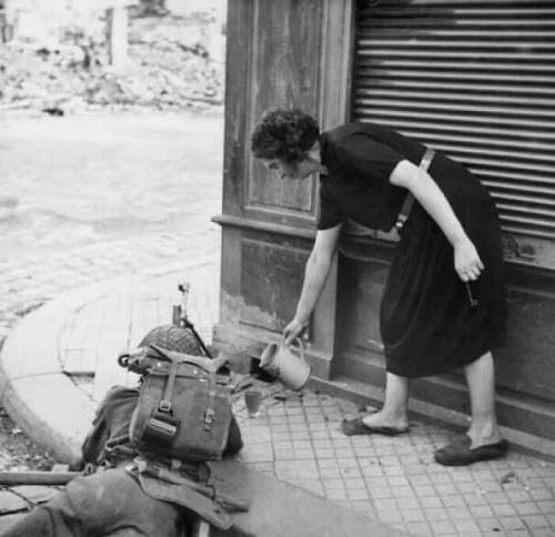 Французская гражданская женщина наливает сидр британскому солдату с пулеметом Брен в Лизье, 1944 год.